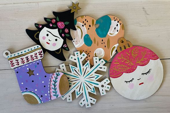 various painted wooden holiday ornaments including a stocking and a snowflake