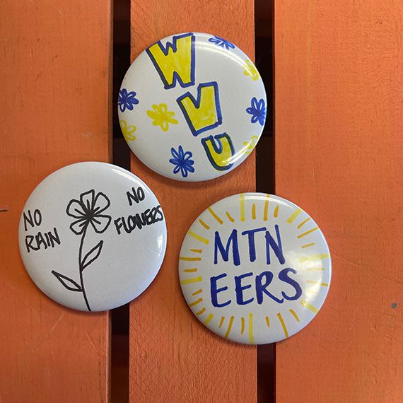 custom made button with flowers, "WVU" and Mountaineers drawn on them.