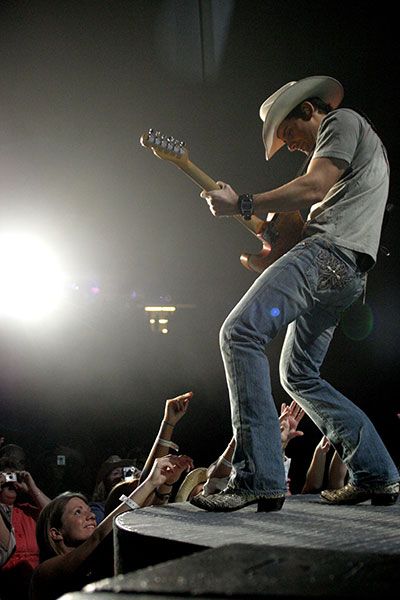 Brad Paisley performing at the front of the Coliseum stage with fans in the front row singing along.