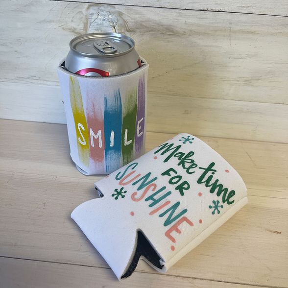 White drink koozies painted with colorful messages. One reads "smile" and one reads "Make time for Sunshine."