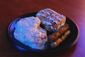 Plate of sausage gravy over biscuits, sausage links and an iced pastry.