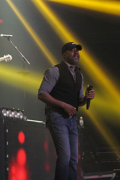 Darius Rucker holds his microphone on stage with yellow spotlights raining down