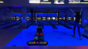 A Bowler raises their arms to celebrate their score. Lanes are lit in blue.