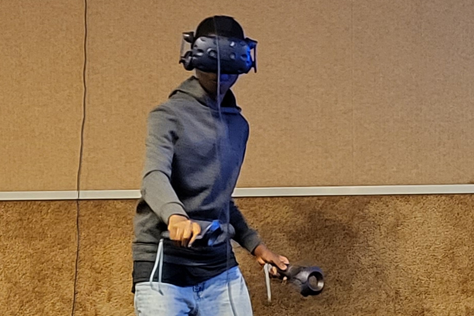 A student wearing a grey hoodie plays virtual reality game