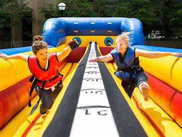 Two female players run along an inflatable chute with a bungee cord attached to the vests they are wearing.
