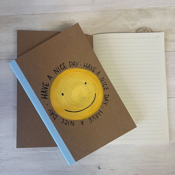 Lined paper notebook. Brown cover is painted with a yellow smiley face.