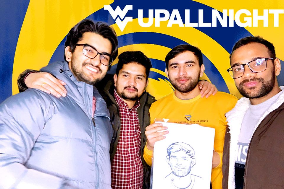 Four students gather for a photo. One is holding up a caricature portrait.
