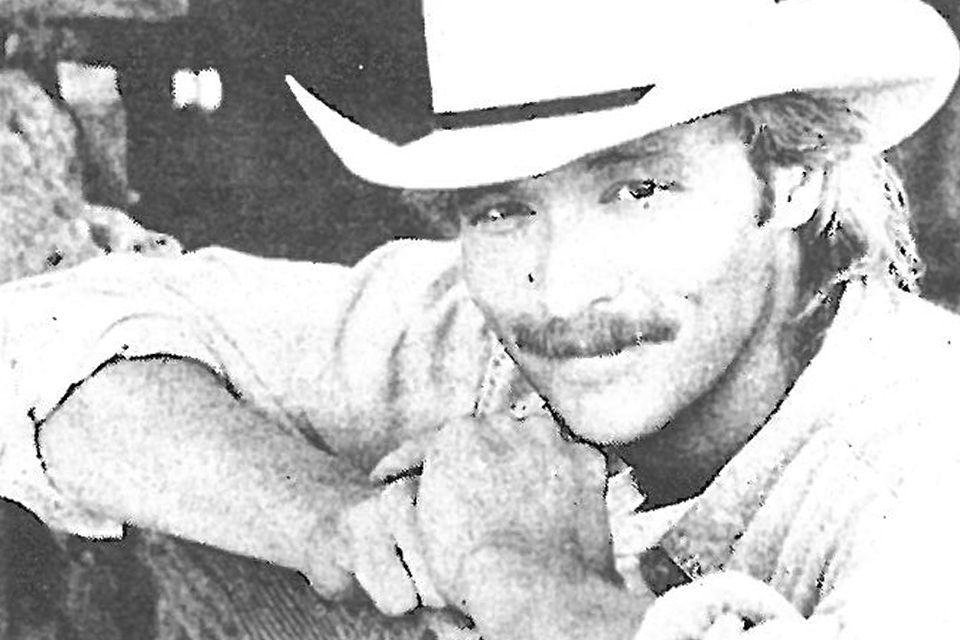 Photo of Alan Jackson with his guitar and his signature white cowboy hat.