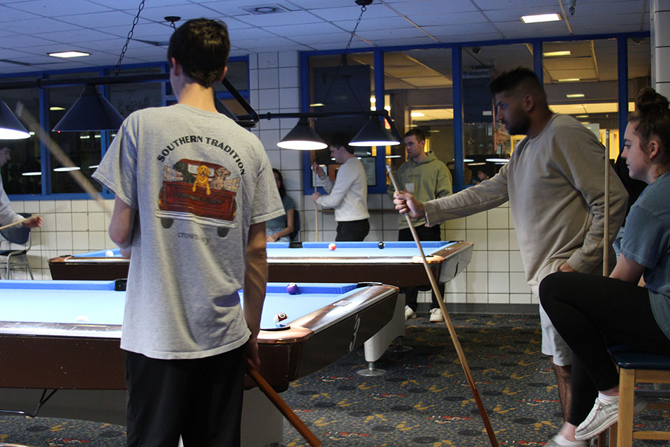 A group of student hold pool cues standing next to a pool table.